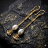 Long gold chain dangler earrings featuring a large white baroque pearl and tiny cluster beads at the base.