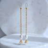 Pair of dainty long gold earrings with white pearls hanging over a marble pedestal.