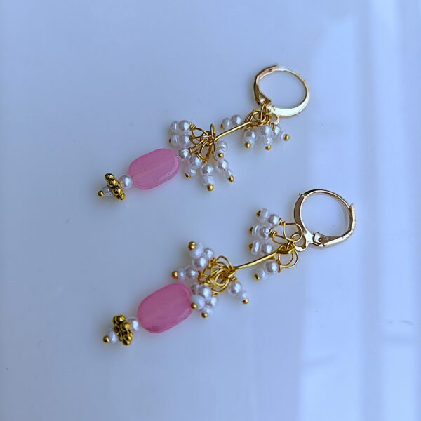 Close-up of handmade pink stone earrings with intricate gold wire wrapping and pearl clusters.