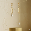 Minimalist jewelry photography of mismatched gold and pearl earrings hanging on a thin wire above a gold metallic cube.