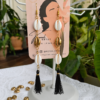 Product shot of long cowrie shell earrings with 18 K Gold plated details and black tassels.