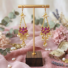 18k gold-plated chandelier earrings featuring lotus-shaped purple Kundan motifs and delicate pearl cluster drops displayed on a wooden stand.